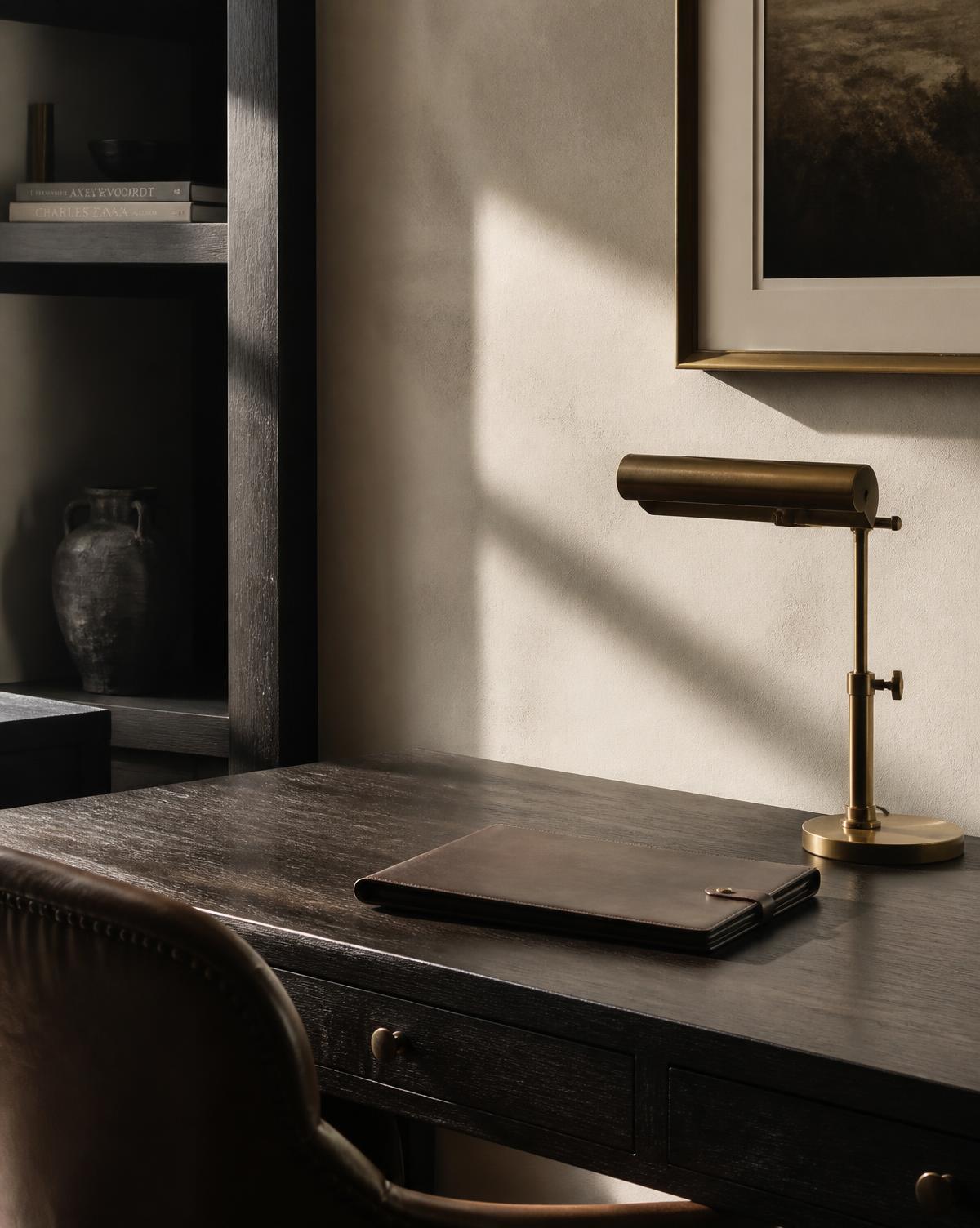 Quiet home office with a dark timber desk, leather folio and brass lamp in afternoon light